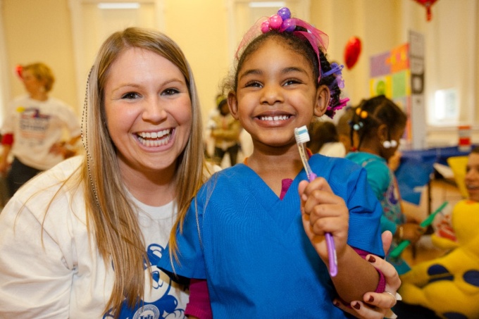 A student volunteer smiles with a young child holding a toothbrush. 