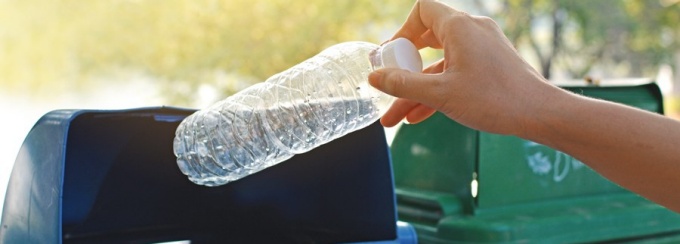 A hand dropping a plastic water bottle in a recycling bin. 