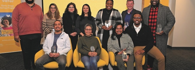 Cultivator graduates pose while sitting and standing behind a projection that says Cultivator. 