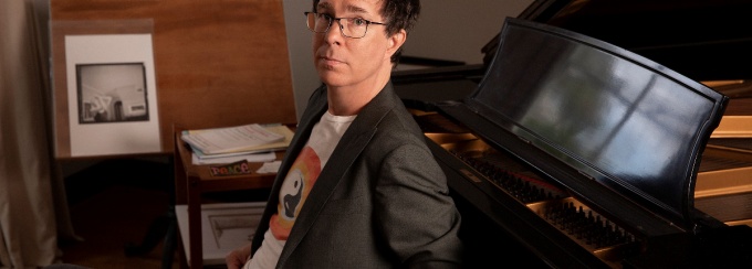 Ben Folds sits at a piano. 