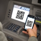 Man comparing QR code on a smartphone with one on an ATM machine. 
