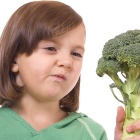 Young girl looking skeptically at a head of broccoli. 