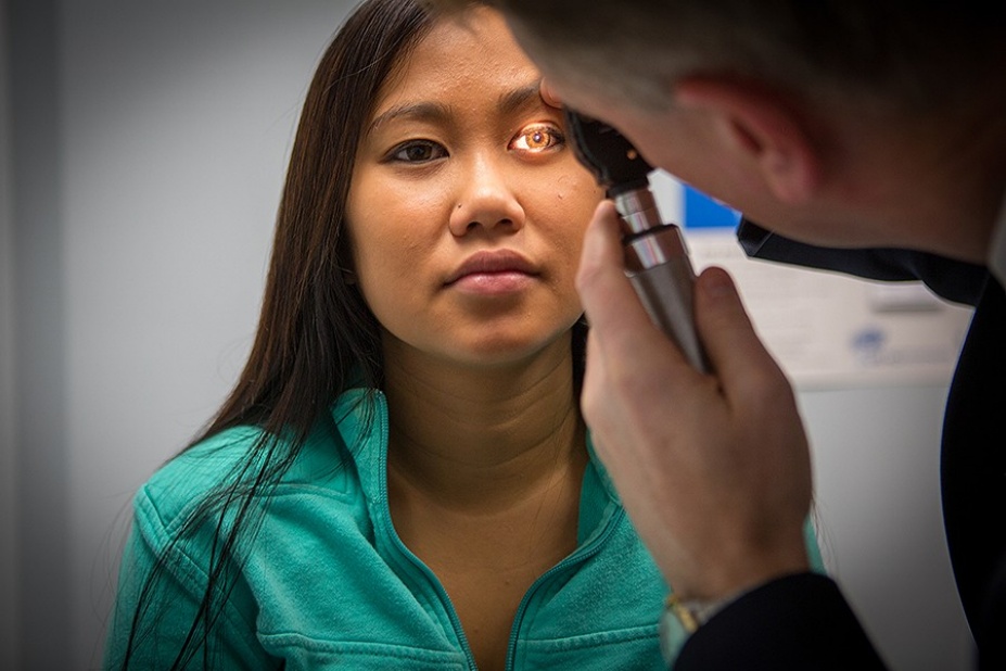 Physician examines patient's eyes with lighted instrument.