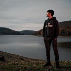 Mikaj Karki, wearing a UB Bulls "Buffalo" sweatshirt, stands in front of a lake with hills in the background. 