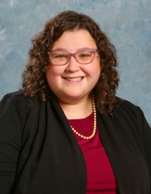 Anna Lawrence smiling with curly hair and glasses wearing a pearl necklace. 