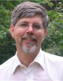 James Jensen smiles. He has shorter hair and a goatee, and is wearing glasses and a button down shirt. 