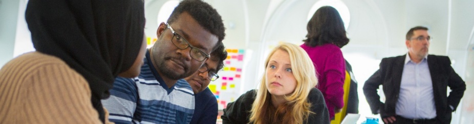 Students working in a group with people standing in the background. 
