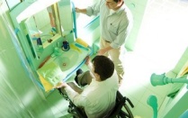 Overhead view of a person in a wheelchair in front of a sink with another person standing to the right. 