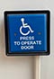 Blue switch with white lettering that reads press to operate door. 
