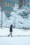 A person walking on campus with snowy areas in the foreground and background. 
