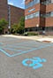Two accessible parking spaces with an access lane in between and a campus building in the background. 