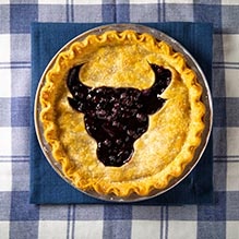 Overhead view of a blueberry pie with the UB Bulls spirit mark cut out of the top crust. 