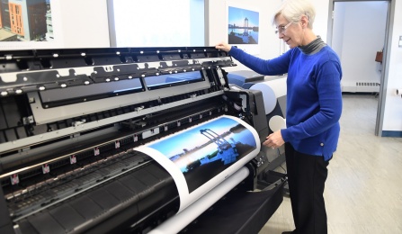UB Print Services staff member stands near large printing machine. 