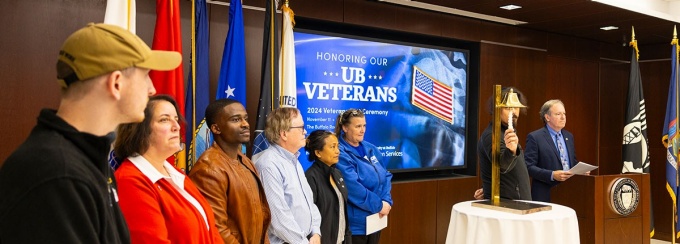 UB Veterans standing in a line being recognized by a speaker at a podium. 