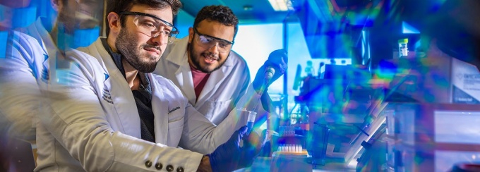 two researchers in white lab coats working with test tubes. 