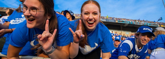 Two fans in the stands holding up horns up hands. 