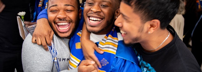 a graduate in commencement robe being hugged by two friends. 