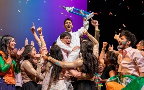 Students celebrating on a stage with confetti and holding up a trophy. 