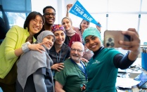 Photo of UB staff members gathered around a sitting staffer for a selfie taken by one of the group. 