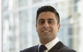 Ali Alipour stands smiling with folded arms wearing a suit. 