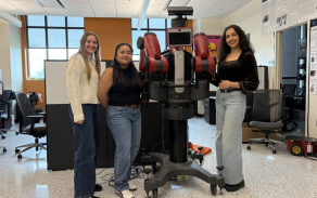 Heather Amistani, Denielle Oliva and Behnoush Hatami pose with Manuel, a robot in David Feil-Seifer's lab. 