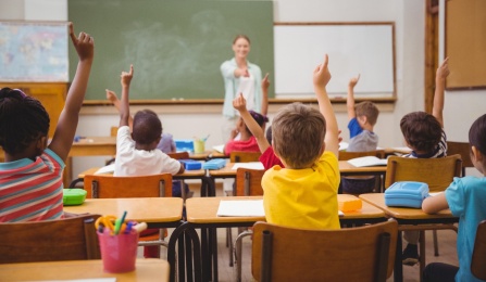 Children raising their hands in a classroom. 