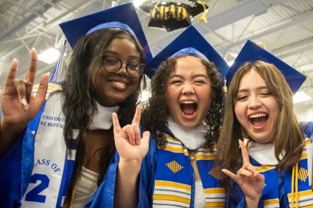 Three UB grads putting their horns up after a commencement ceremony. 