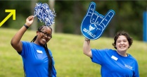 Zoom image: Two UB students one with a blue foam finger and one with a blue and white pom-pom