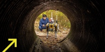 Zoom image: UB student guiding a robot dog into a culvert 