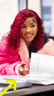 Zoom image: UB student sitting at a desk with books and papers 