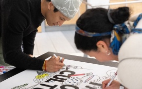 Two people colr in portions of a poster. 