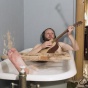 Still Image from Video by Ragnar Kjartansoon of a man with headphones in a bubble bath playing guitar with his right leg stretched out of the bath tub. 