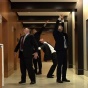Photograph of four male figures in black suit stretching in the office hallway. 