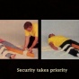 Sill Image from Video by Kelly Sears juxtaposing two images; woman with pink shirt lying on the floor and the man on the right applying a bandage on woman's left leg with wooden stick(left image), man with yellow shirt lying on the floor with a woman on the right applying a bandage with wooden stick on the man's left leg(right image) and 'Security takes priority' on the bottom center of the still. 