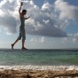 Photography by Janine Antoni of a person with arms rasied walking on a tightrope that is aligning with the horizon of the ocean on the back. 