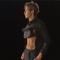 A photo of a man in profile. He wears a black shirt that is pulled up in front, revealing very tight abs. 