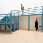 A photo of Heather Hart's sculpture, Sweet Lorraine, installed in UB CFA Gallery lightwell. Two figures stand under and around the sculpture, while one figure stands on the sculptural balcony. 
