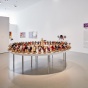 An installation image of Thinking in Indian at UB CFA Gallery. In the foreground is a work by Elizabeth Doxdater where atop large, circular table hundreds of cornhusk dolls are arranged. In the background is a title wall that reads "O&rsquo;nig&ouml;&euml;i:yo:h Thinking in Indian.". 