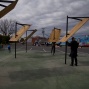 A series of sculptures are installed in a parking lot. The sculptures are about 12feet high, with steel armatures that are mounted in the ground. they have sheets of plywood attached to them at a 45 degree angle that catch the sun. 