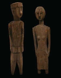 Two wooden funerary figures. They are made of wood and tall and thinly sculpted. The figure on the right looks to be feminine with small breasts. 