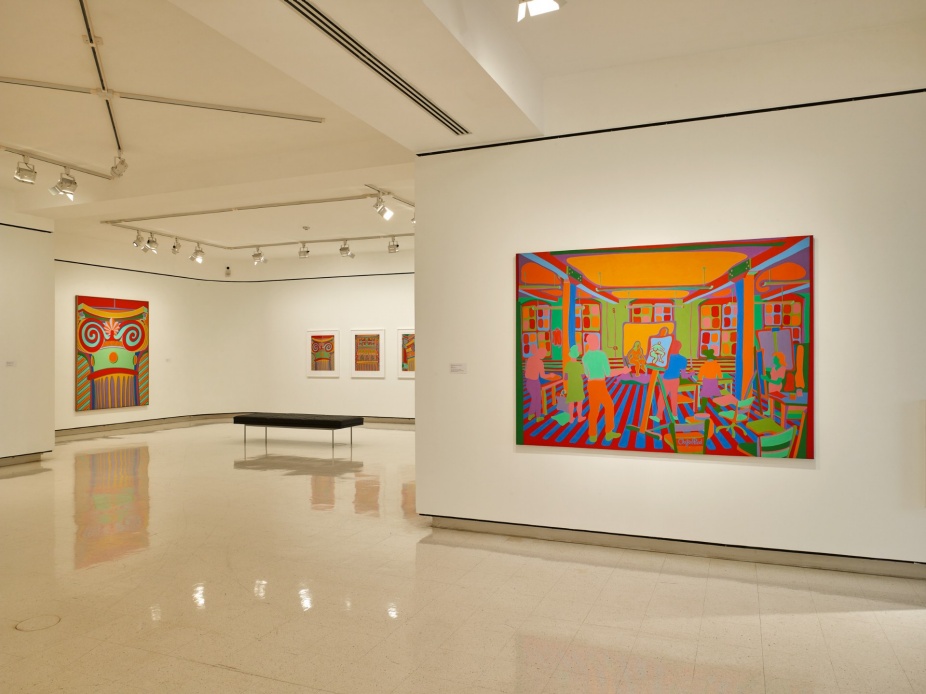 Installation view of Clayton Pond: A Retrospective at UB Anderson Gallery, University at Buffalo. The gallery features white walls and a polished terrazzo floor. On the right wall hangs a large painting depicting a colorful interior scene with figures gathered around an easel in an art studio, rendered in saturated oranges, reds, greens, and blues. On the far left wall, a tall vertical painting shows a stylized Ionic column in bold red and teal stripes. In the background, three smaller framed works are displayed in a row. A low black upholstered bench sits in the center of the gallery floor. Photo: Biff Henrich. 