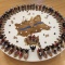 A photo of a work by Elizabeth Doxtater. On a white round table a circle of corn husk dolls in boats faces outward. In the center of the circle is a cow hide and more corhnusk dolls arranged in ceremony. 