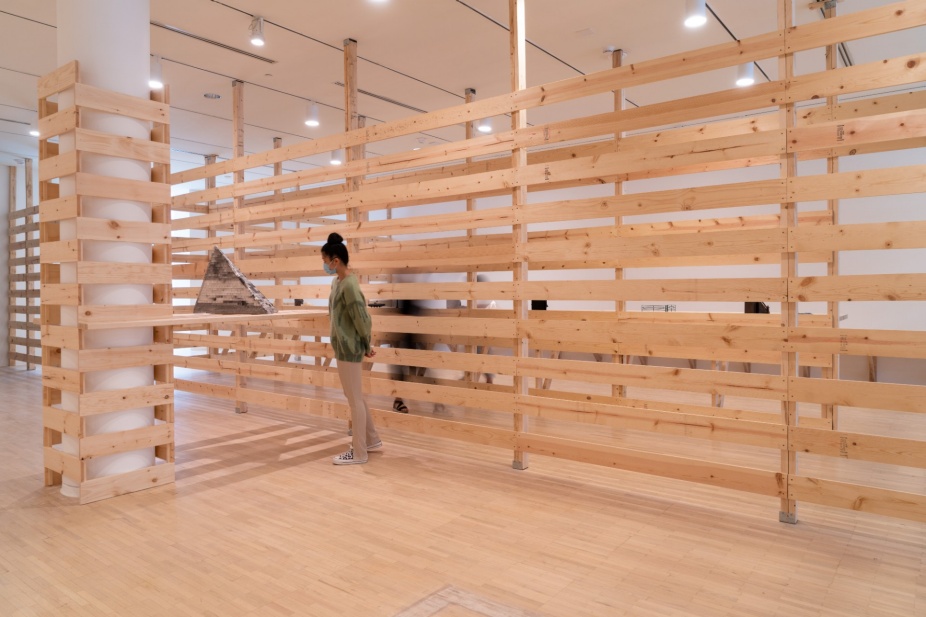 An installation photo of Heather Hart: Afrotecture Re(Collection) where a visitor is looking at an artwork that looks like a pyramid on a shelf. 