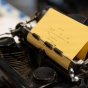 A vintage black typewriter with yellow paper loaded, showing a typed poem with partially legible text including the words 'alone,' 'body,' and 'promise of death.' The word 'Silent' is visible on the typewriter's body. 
