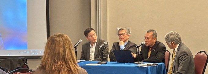 Four people at a table speaking to an audience inside. 