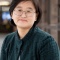 Woman with short hair and glasses wearing a dark teal jacket. 
