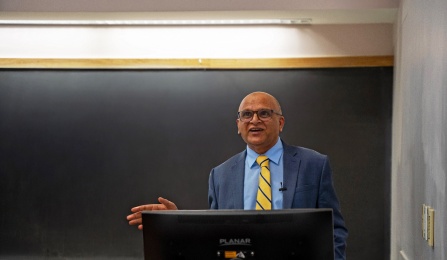 Man in a suit presenting in front of a blackboard. 