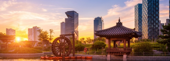 Korean traditional pavilion and water wheel by a river at sunrise with skyscrapers in the background. 