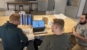 Three people collaborating at a table with a laptop and architectural models. 