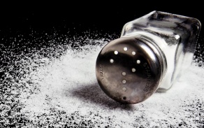 Salt shaker on it side surrounded by salt. 